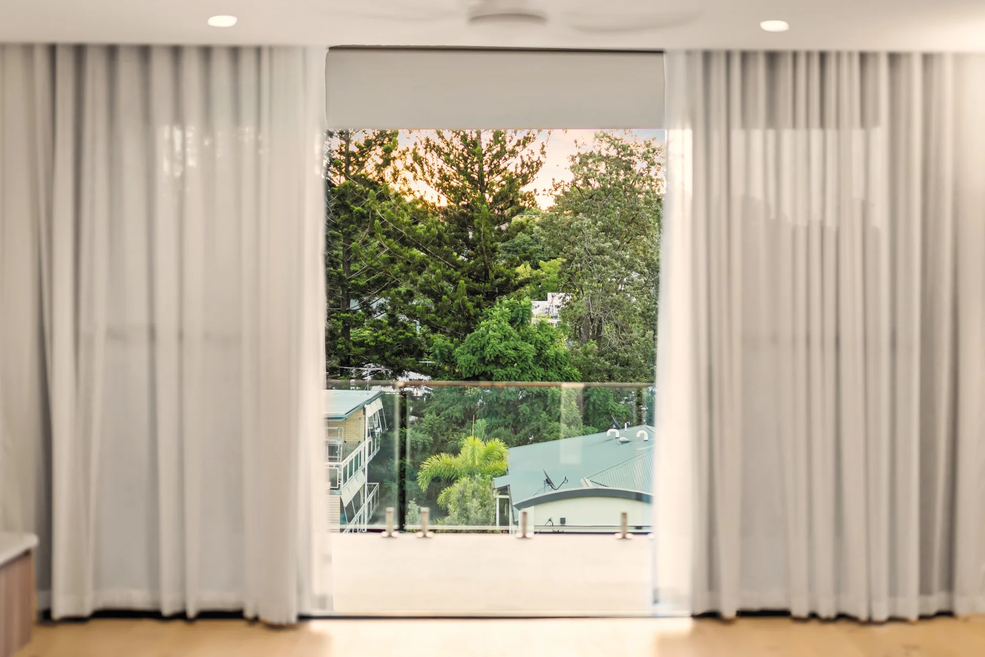 Sheer curtains drawn back to a balcony and the tree canopy beyond, at Holland Residences